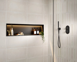 A modern shower niche with light beige rectangular wall tiles, a black backlit shelf, and black shower fixtures including a handheld shower head and control valve on a glass door.