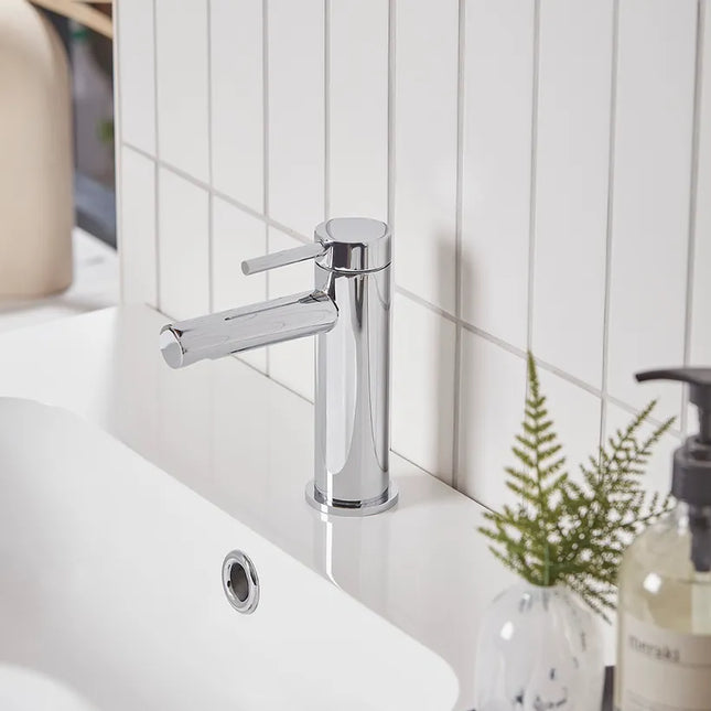A modern single-handle bathroom faucet with a polished chrome finish, mounted on a white sink against a white tiled wall.