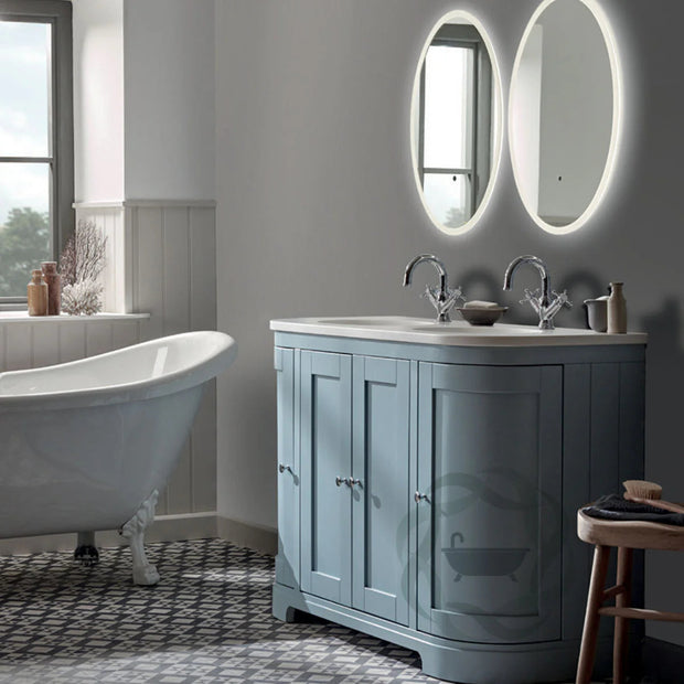 Bathroom with a blue vanity, white freestanding bathtub, and oval mirrors.